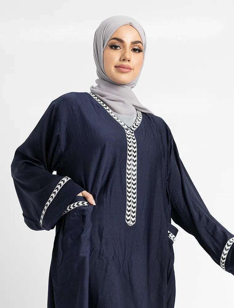 Woman wearing a navy blue dress with white embroidery on a light gray background
