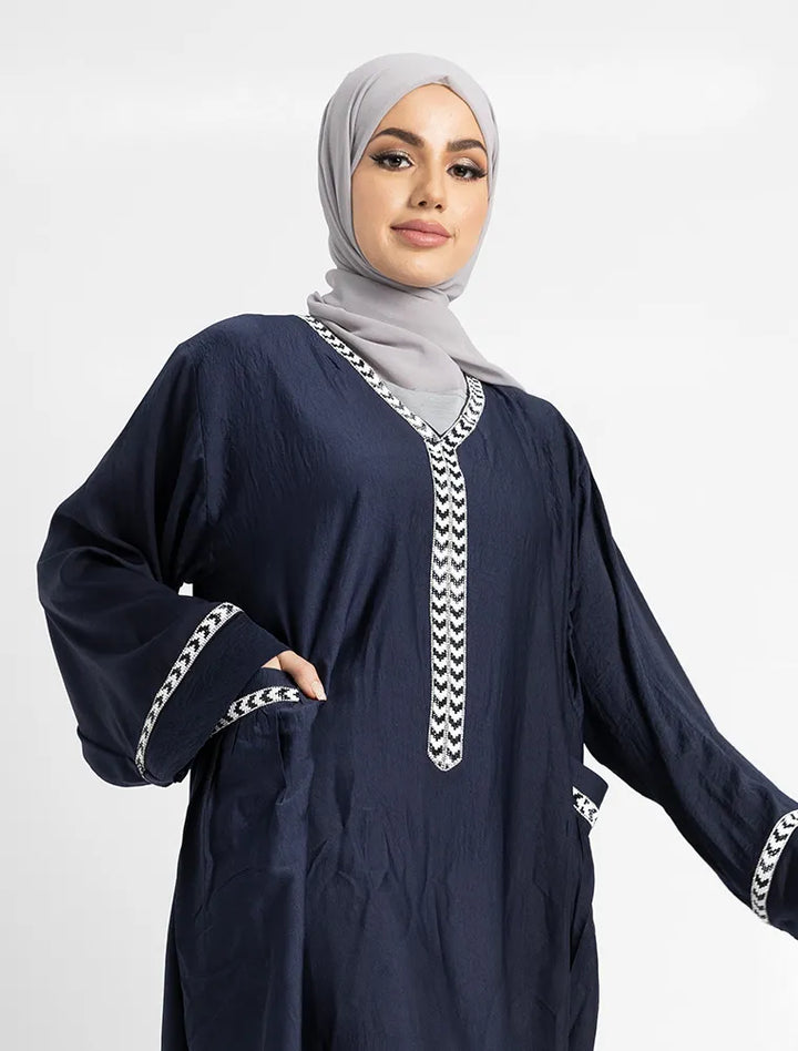 Woman wearing a navy blue dress with white embroidery on a light gray background