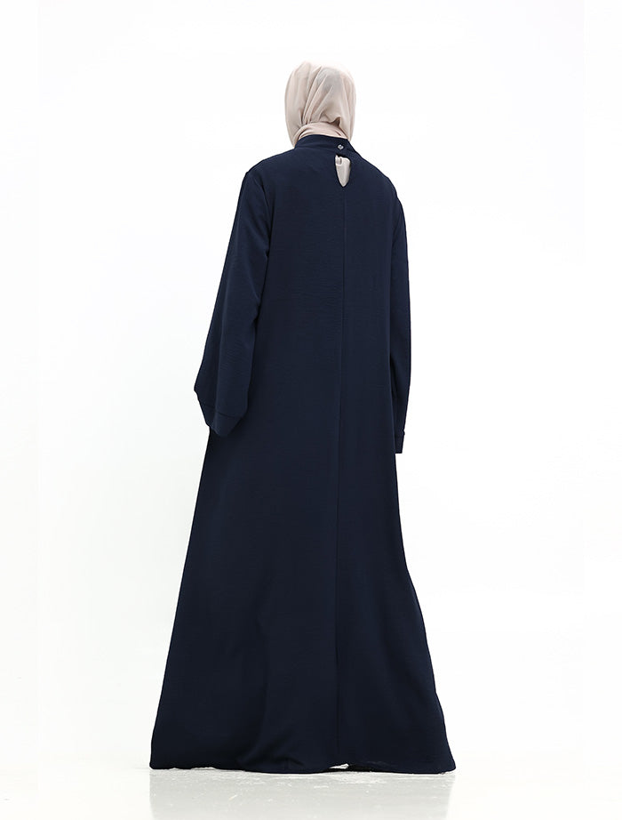 A woman wearing a long, dark navy abaya with a high collar and a light beige hijab, shown from the back against a plain white background.