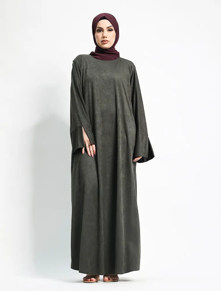 A woman modeling a long, loose-fitting dark gray abaya dress with wide sleeves, paired with a deep burgundy hijab, standing against a plain white studio background.