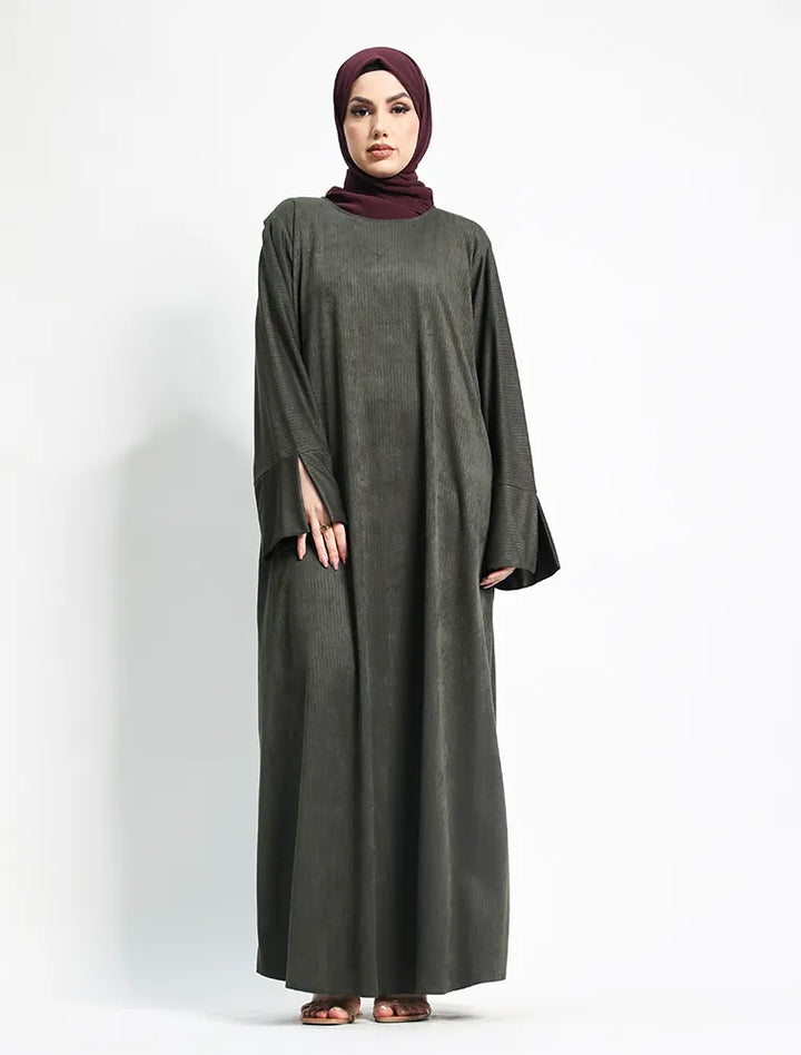 A woman modeling a long, loose-fitting dark gray abaya dress with wide sleeves, paired with a deep burgundy hijab, standing against a plain white studio background.
