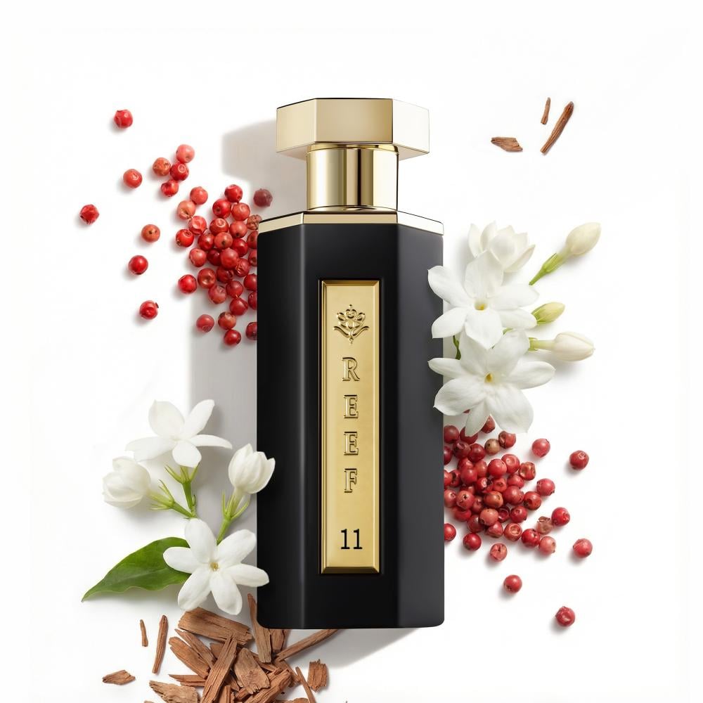Perfume bottle with gold cap and black body, surrounded by red berries and white flowers on a white background