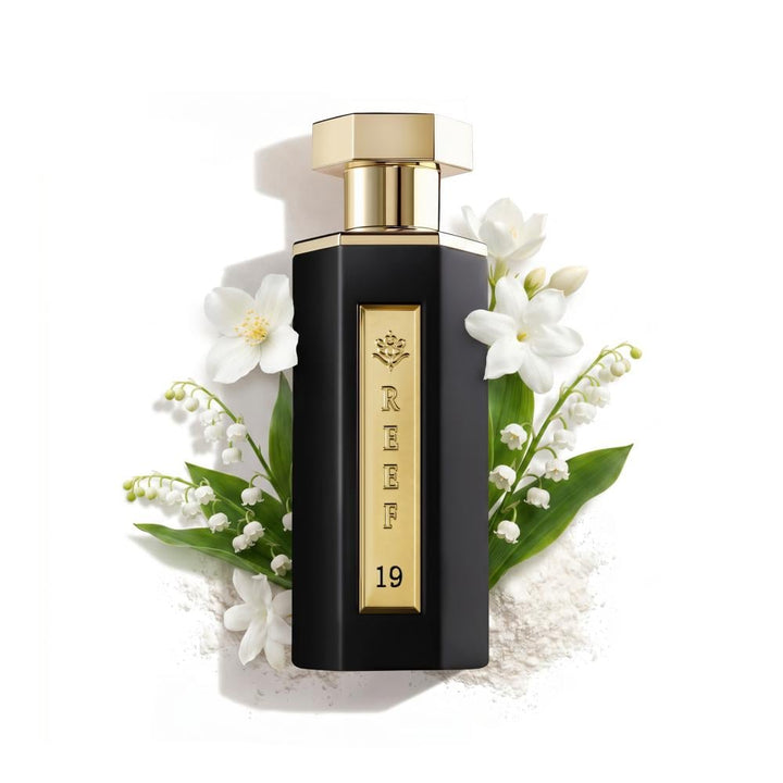 Perfume bottle with gold cap and black body surrounded by white flowers on a white background