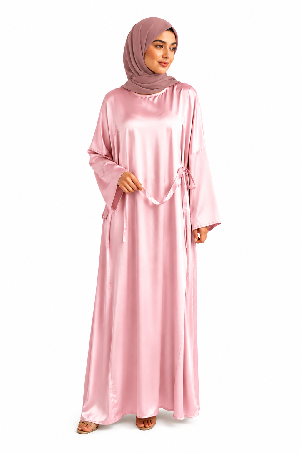 A woman modeling a long, flowing pink abaya with a matching headscarf, standing against a plain white background.