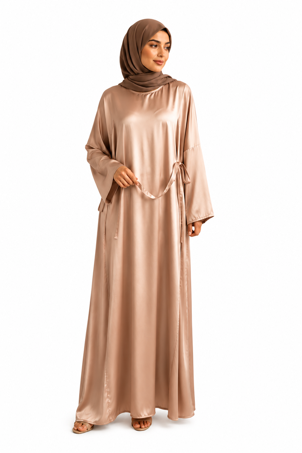 A woman modeling a long, flowing abaya dress in a shiny taupe-brown satin-like fabric, paired with a matching hijab, against a plain white background.