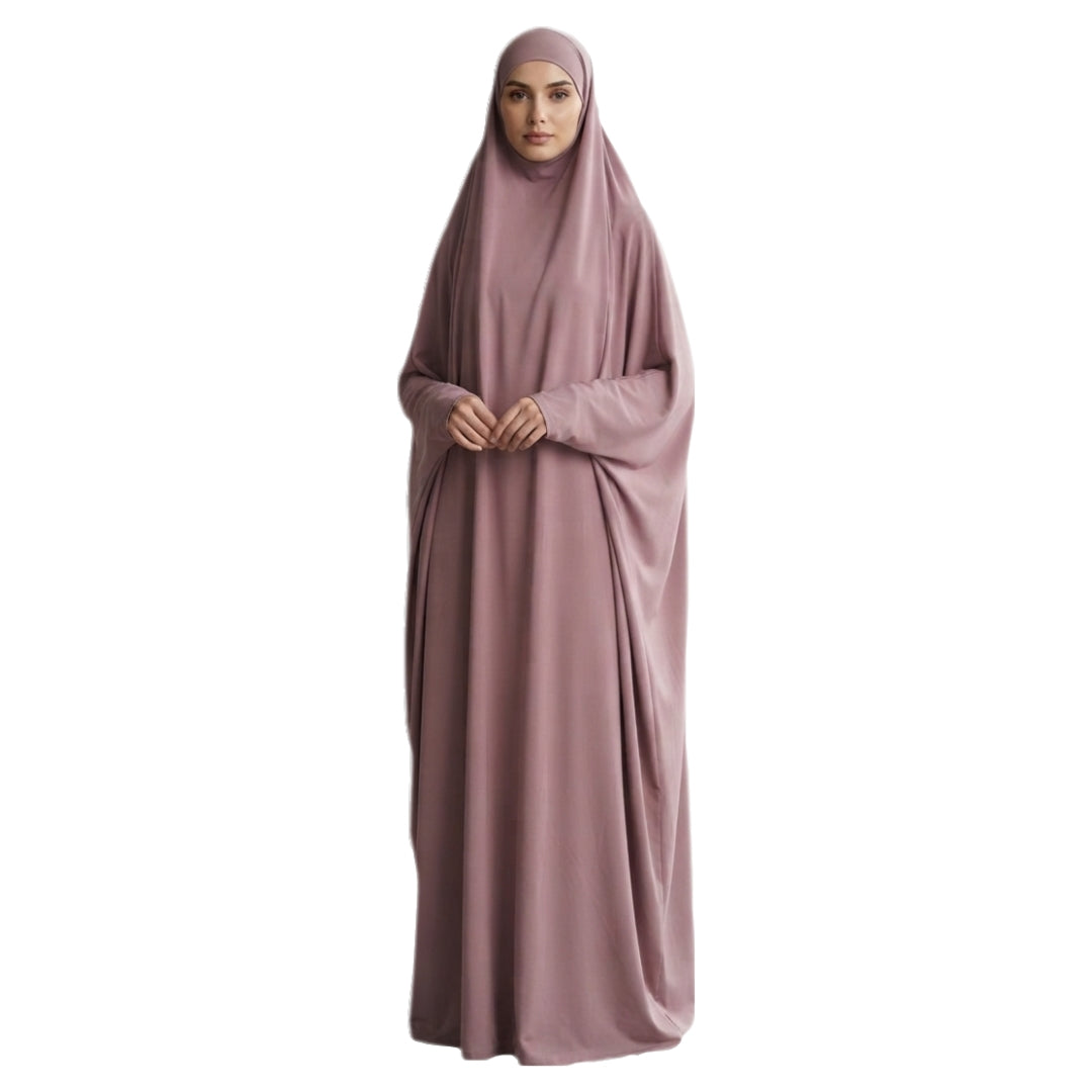 A woman wearing a modest, floor-length dusty rose abaya with a matching hijab, standing against a plain white background.