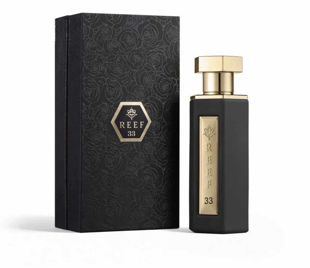 A black rectangular perfume bottle with gold trim and a gold cap stands beside its matching black presentation box, both featuring the brand name REEF 33 in gold on a clean white background.